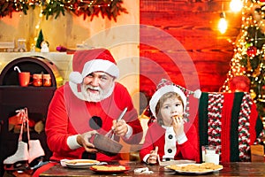 Christmas bakery. Kid Santa Claus enjoying in served gingerbread cake and milk. Santa Father and son having fun near