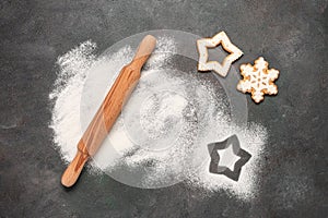 Christmas baking background. Flour, rolling pin and gingerbread on dark grunge background. Top view, flat lay.