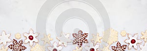 Christmas baking bottom border with a variety of snowflake cookies on a white marble background