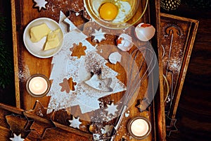 Christmas baking composition, fir tree shape from flour, butter, egg and cinnamon stars, utensils and candles on warm brown wooden