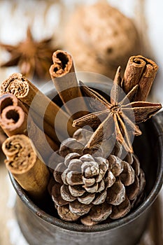 Christmas Baking Ingredients Cinnamon Sticks Anise Star Walnuts Cloves Pine Cone in Vintage Jug on Wood Background