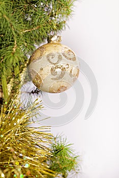 A Christmas ball with golden sparkles hangs on a branch of a natural Canadian Konica Christmas tree, close-up, selective focus.