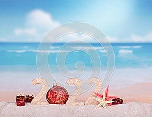 Christmas ball and New Year`s gifts on the beach. Figures 2022 on sea sand