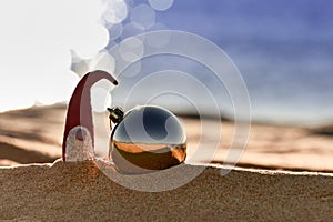 Christmas ball and Santa Claus or dwarf on beach against background of sea. New Year and Christmas celebration concept