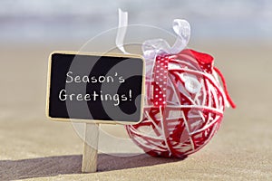 Christmas ball and text seasons greetings on the beach