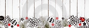 Christmas banner of black and white checked buffalo plaid ribbon, gifts and ornaments, above view bottom border on a white wood ba