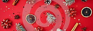 Christmas banner composition. Fir branches, pine cones, dried fruits and festive confetti on a red background, top view