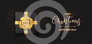 Christmas banner. Gift box decorated with gold bow-ribbon isolated on black background.