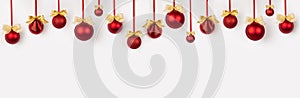 Christmas banner in modern simplicity style - shiny red balls with gold bows hang on ribbon in row as pattern on white wall.