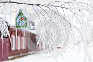 Christmas barn birdhouse covered in snow with snow covered trees blurred in background
