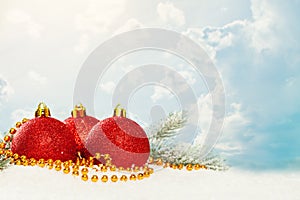 Christmas baubles, gold garland and green fir branch on white snow against blue sky with white clouds. Winter holidays background