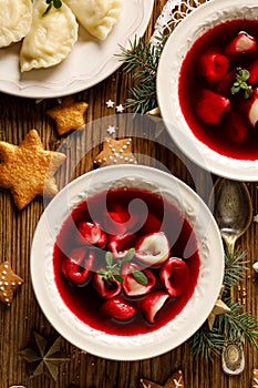 Christmas beetroot soup, borscht with small dumplings with mushroom filling in a ceramic bowl on a wooden table, top view.