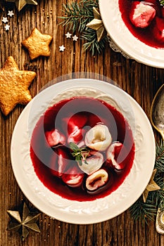 Christmas beetroot soup, borscht with small dumplings with mushroom filling in a ceramic bowl on a wooden table, top view.