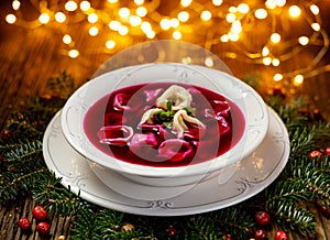 Christmas beetroot soup, red borscht with small dumplings with mushroom filling in a ceramic white plate on a wooden table