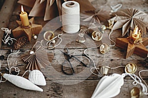 Christmas bells, paper angel, stars, candle, thread, scissors on rustic wood. Making scandi decor