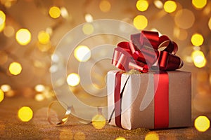 Christmas or Birthday gift box with red ribbon against golden lights and bokeh background. Holiday greeting card