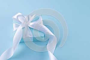 Christmas blue background. Holidays gift box wrapped in blue paper with white ribbon bow on blue background