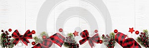 Christmas border banner of ornaments, branches and red and black checked buffalo plaid ribbon, top view on white wood