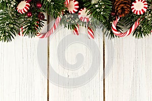 Christmas border of branches and candy canes on white wood