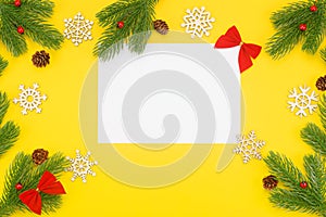 Christmas border with branches of spruce, mountain ash, cones and a blank white paper on a yellow background