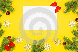 Christmas border with branches of spruce, mountain ash, cones and a blank white paper on a yellow background
