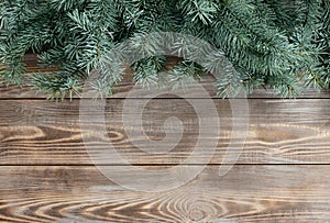 Christmas border with fir branches on a brown wooden background. Festive greeting card with space for text. Top view, flat lay