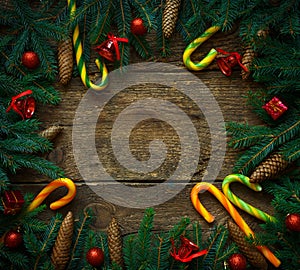 Christmas border with fir tree branches, cones, christmas decorations and candy cane on rustic wooden boards