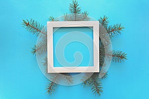 Christmas Border. Fir tree branches and white wooden frame on blue paper background. Top view. Copy space.