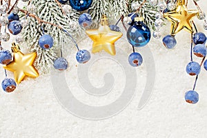 Christmas border of gold star decor, green fir branch, blue berries and baubles on winter white snow background. Xmas and New Year