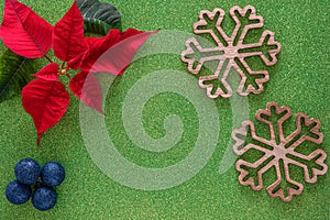 Christmas border with red poinsettia flowers in corner and two large wooden snowflakes, blue festive balls on green glitter paper