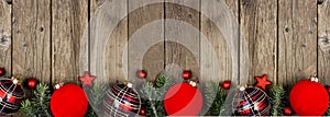 Christmas border of red and shiny plaid ornaments with tree branches on a rustic wood banner background