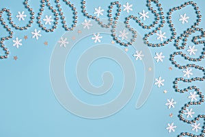 Christmas border with silver garland and stars, white snowflakes on pastel blue background. Space for text. Winter concept