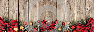 Christmas bottom border of ornaments, branches and buffalo plaid check ribbon on an old wood banner background