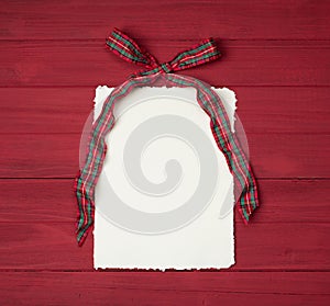 Christmas Bow that is Red and Green plaid with Vintage Paper with ragged edges on Rustic Wood Boards Background with copy space
