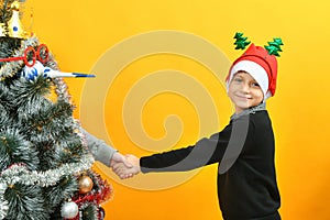 Christmas boy greets the Christmas tree by the hand on the holiday, miracles and magic on New Year`s Eve