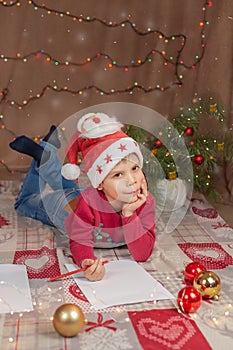 Christmas boy writing letter to Santa Claus. Christmas helper child letter in red hat