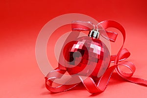 Red toy ball for the Christmas tree with a red ribbon on a red background