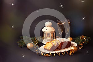 Christmas cake with candied fruits and raison, two glasses of champagne, burning lantern, fir branches and christmas decorations