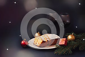 Christmas cake with candied fruits and raison, two glasses of red wine, fir branches and christmas decorations on dark background