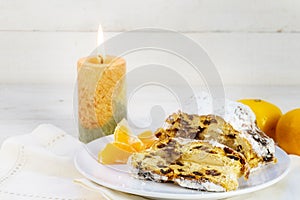 christmas cake, german christstollen with tangerines and a burning candle against a white wooden background with copy space