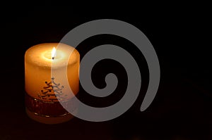 Christmas candle burning in the night. Thick handmade candle with Christmas tree design burning over black background