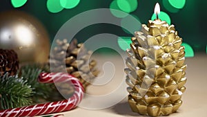 Christmas candle in gold color in the shape of a pine cone and New Year decorations around. Night.