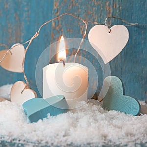 Christmas candle in white with blue hearts, wood and snow for de