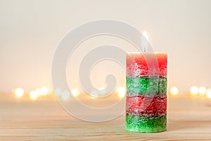 Christmas candle on wooden table with defocused holiday lights in background