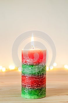 Christmas candle on wooden table with defocused holiday lights in background