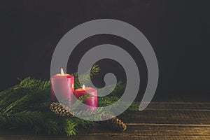 Christmas candles and lights. Two burning candles with fir branch and cones over wooden background, still life