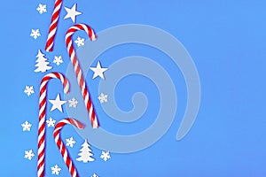 Christmas candy cane lied evenly in row on blue background with decorative snowflake and star. Flat lay and top view