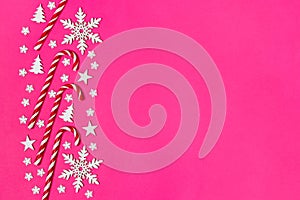 Christmas candy cane lied evenly in row on pink background with decorative snowflake and star. Flat lay and top view