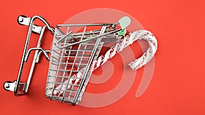 Christmas candy cane in shopping cart. red background. Flat lay, top view, copy space