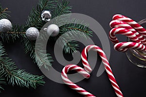 Christmas candy cane with silver evening balls and green fir tree on black background. Christmas concept. Top view and copy space,